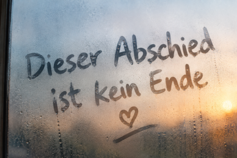 Auf einem beschlagenen Fensterglas steht geschrieben „Dieser Abschied ist kein Ende“, darunter ist ein Symbol in Herzform auf dem Glas zu erkennen.