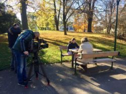 Freizeitassistenz und Jugendcoaching check.IN Teilnehmerin Larissa wird von einer Journalistin des ORF interviewt. Die beiden Frauen sitzen in einem Park auf einer Bank. Neben ihnen stehen der Kameramann und der Tonmann. Es ist ein sonniger Herbsttag.