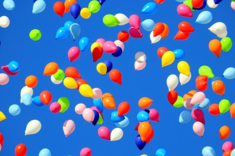 Auf dem Foto sieht man viele bunte Luftballons vor einem blauen Himmel.