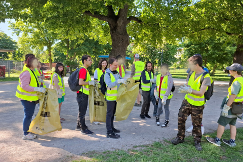 Die Teilnehmer*innen des Projekt P.I.L.O.T. stehen mit Müllsäcken und in gelben Warnwesten im Auer-Welsbach-Park und sammeln für die Aktion "Wien räumt auf" gemeinsam liegengebliebenen Müll auf